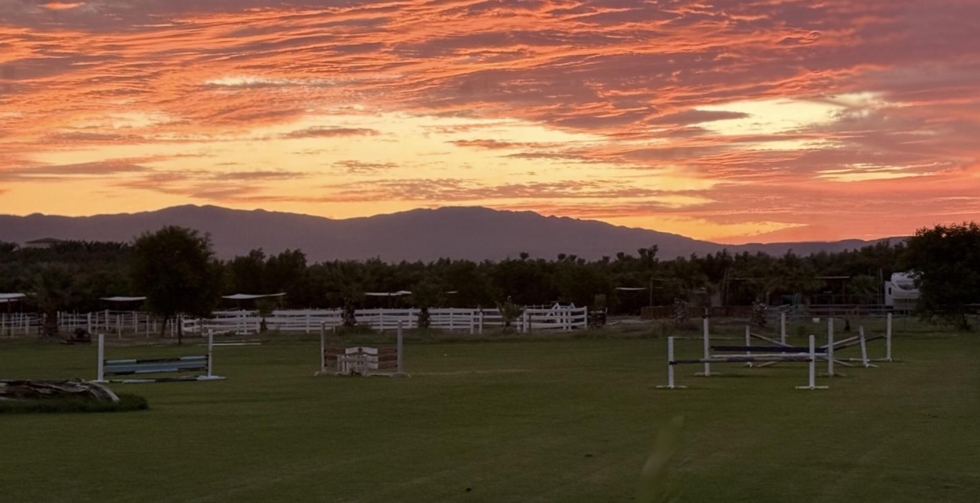 Orange sunset over the Mi Amor Ranch field with white fences and jump equipment