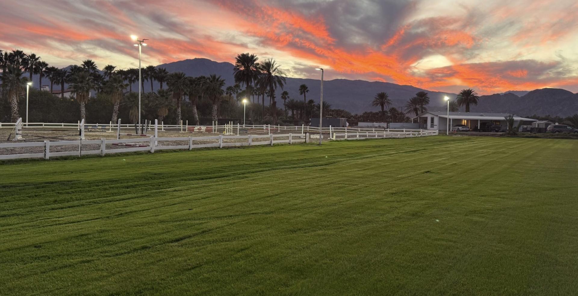 Pink and orange sunset over the Mi Amor Ranch polo field with white fences and palm trees